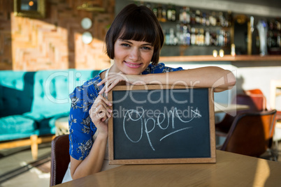 Smiling woman sitting in the coffee shop with a open sign