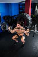 Shirtless man exercising with barbell in gym