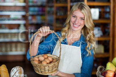 Smiling female staff holding basket of egg in supermarket