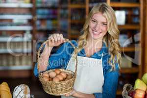 Smiling female staff holding basket of egg in supermarket