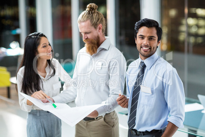 Businessman smiling at camera while colleagues discussing over blueprint