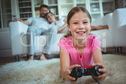 Smiling girl lying on rug and playing video game in living room