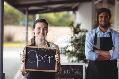 Waiter and waitress standing with chalkboard with open sign