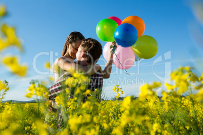 Couple holding colorful balloons and embracing each other in mustard field