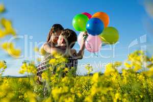 Couple holding colorful balloons and embracing each other in mustard field