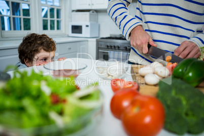 Boy looking while father chopping vegetables