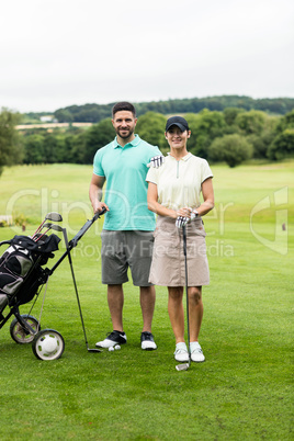 Couple standing with golf club and bag in golf course