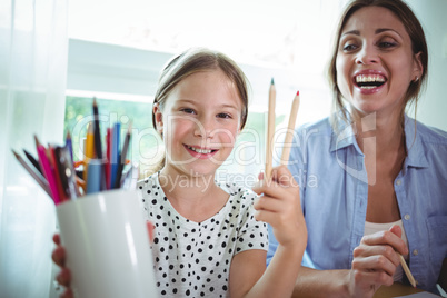 Smiling daughter sitting next to mother and showing color pens