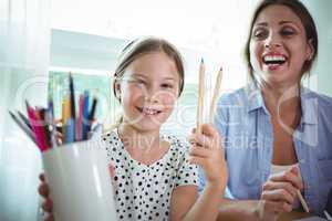 Smiling daughter sitting next to mother and showing color pens