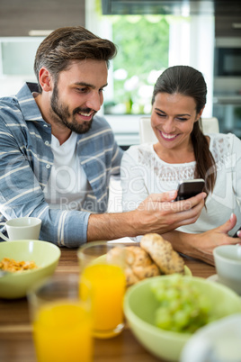 Couple using mobile phone while having breakfast