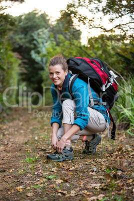 Smiling female hiker tying shoelaces in forest
