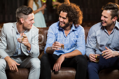Friends interacting with each other while having cigar and whisky in bar