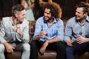 Friends interacting with each other while having cigar and whisky in bar