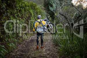 Male biker carrying mountain bike and walking on dirt track