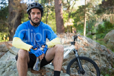 Portrait of male mountain holding water bottle and relaxing on a rock