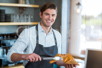 Smiling waiter packing croissant in paper bag at cafÃ?Â©