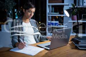 Businesswoman tied with rope while working on laptop at her desk