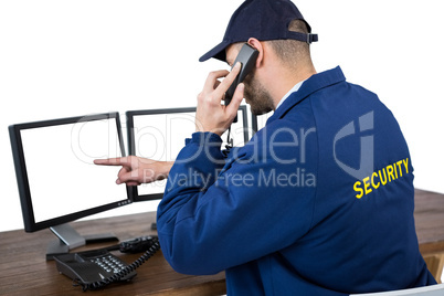 Security officer talking on phone while pointing at computer monitors