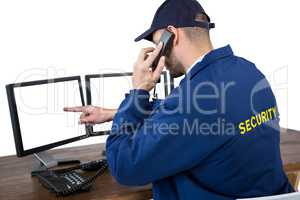 Security officer talking on phone while pointing at computer monitors