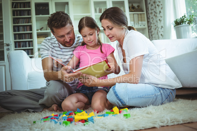 Parents and daughter reading a book while playing with building blocks
