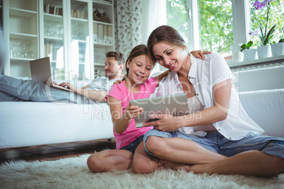 Mother and daughter sitting on floor and using digital tablet