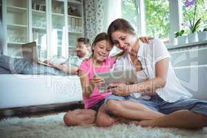 Mother and daughter sitting on floor and using digital tablet