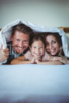 Happy family lying under a blanket on bed
