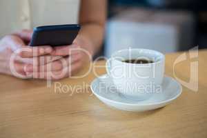 Woman using mobile phone and a coffee cup on the table in coffee shop