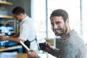 Smiling man using mobile phone while having cup of coffee in cafÃ?Â©