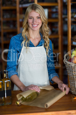 Smiling female staff wrapping olive oil bottle with brown paper