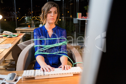 Businesswoman tied with rope while working on computer at her desk