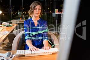 Businesswoman tied with rope while working on computer at her desk