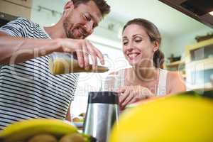 Smiling couple preparing fruit smoothie in kitchen
