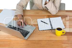 Businesswoman using laptop with diary and black coffee on table