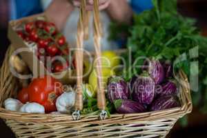 Close-up of female staff holding basket of vegetables in organic section