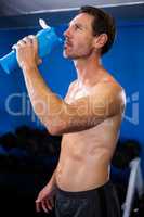 Shirtless young man drinking water in gym