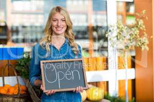 Smiling female staff holding open sign board in super market