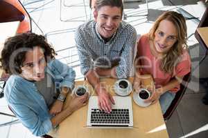 Three friends with coffee cups using a laptop in coffee shop