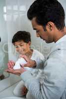 Father spraying shaving foam on hand while son looking