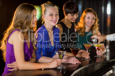 Smiling woman with cocktail standing at counter with her friends