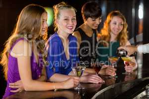 Smiling woman with cocktail standing at counter with her friends
