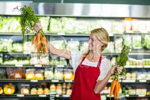 Smiling female staff holding bunch of carrots in organic section