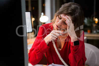 Stressed businesswoman talking on phone at her desk