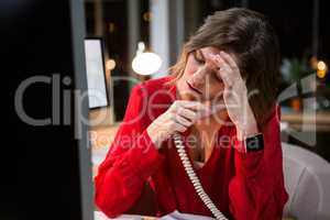 Stressed businesswoman talking on phone at her desk