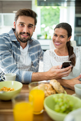 Couple using mobile phone while having breakfast at home