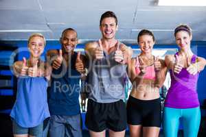 Portrait of smiling friends showing thumbs up in gym