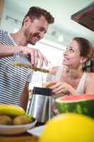 Smiling couple preparing fruit smoothie in kitchen