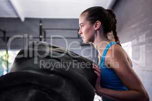 Side view of female athlete pushing tire in gym