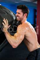 Shirtless male athlete lifting tire