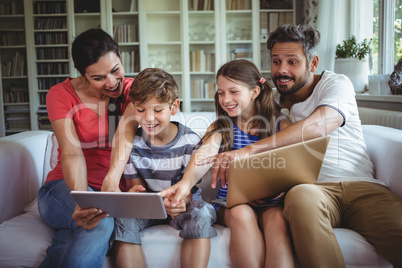 Smiling family sitting on sofa and pointing at digital tablet